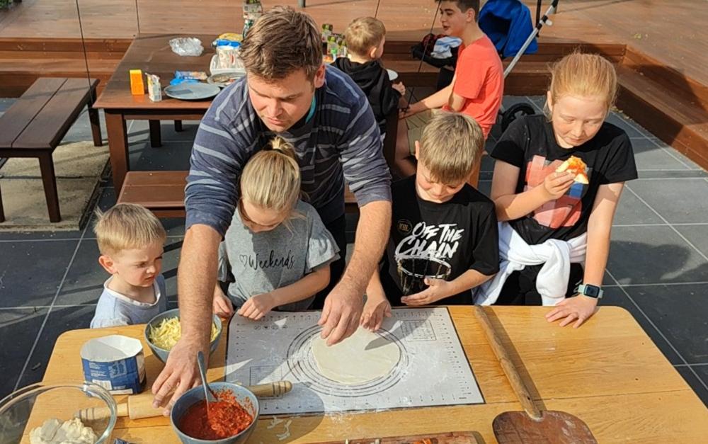 Family preparing homemade pizzas together outdoors for a wood-fired pizza oven
