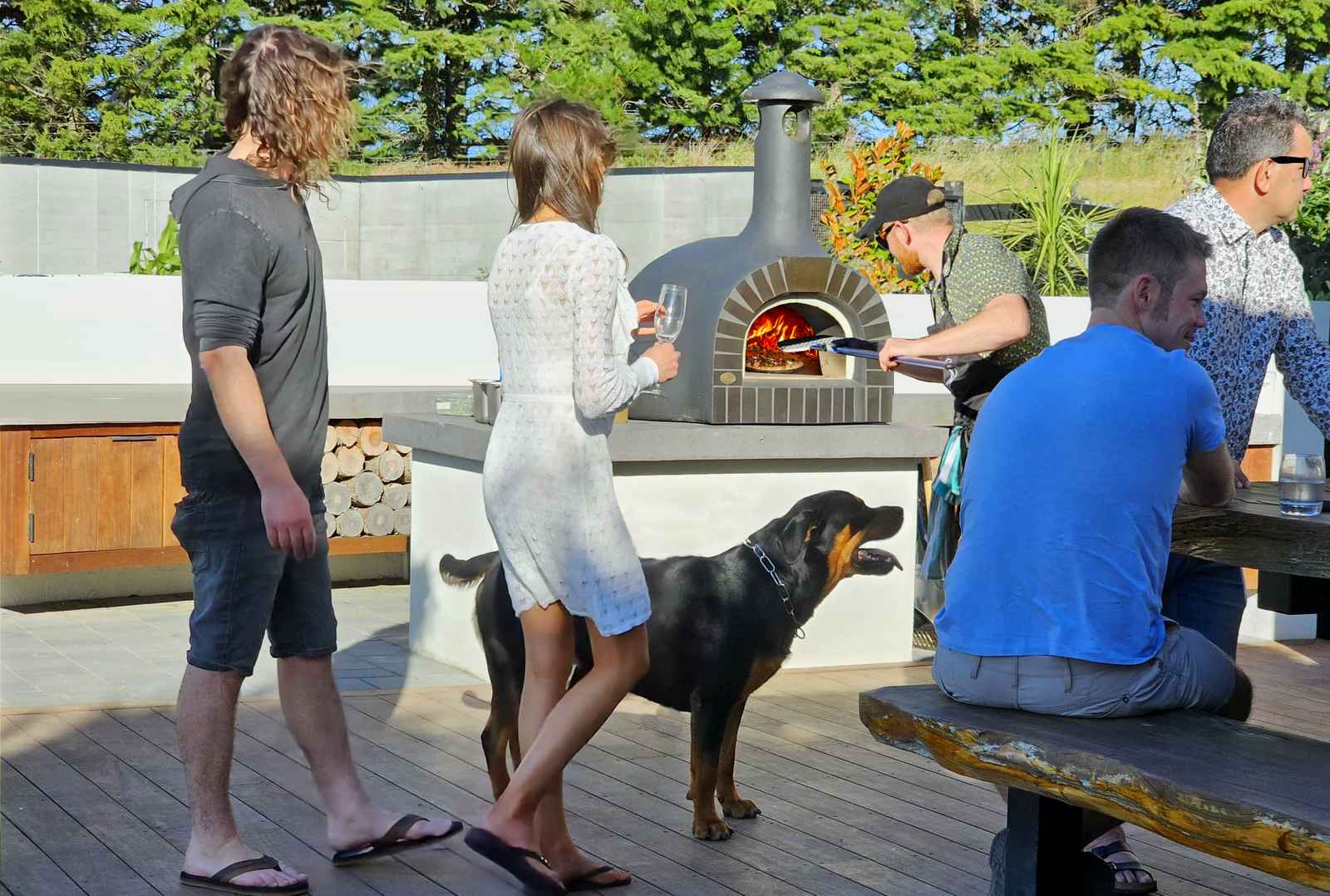 Friends enjoying an outdoor pizza party around a wood-fired pizza oven